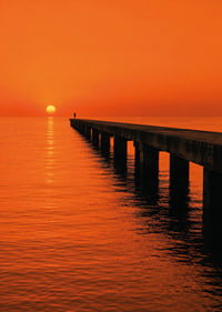 A lone person on a pier in a glowing orange sunset light.-7