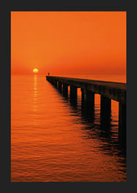 A lone person on a pier in a glowing orange sunset light.-5
