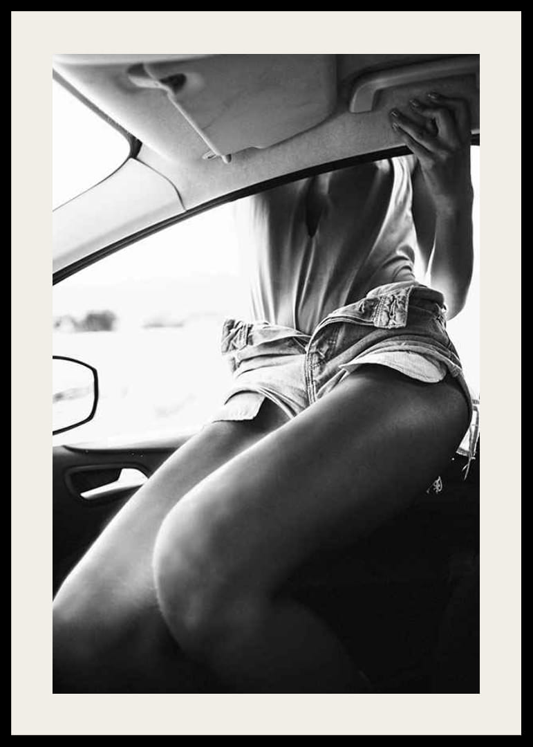 Black and white photo of woman in shorts, sitting in car window-12