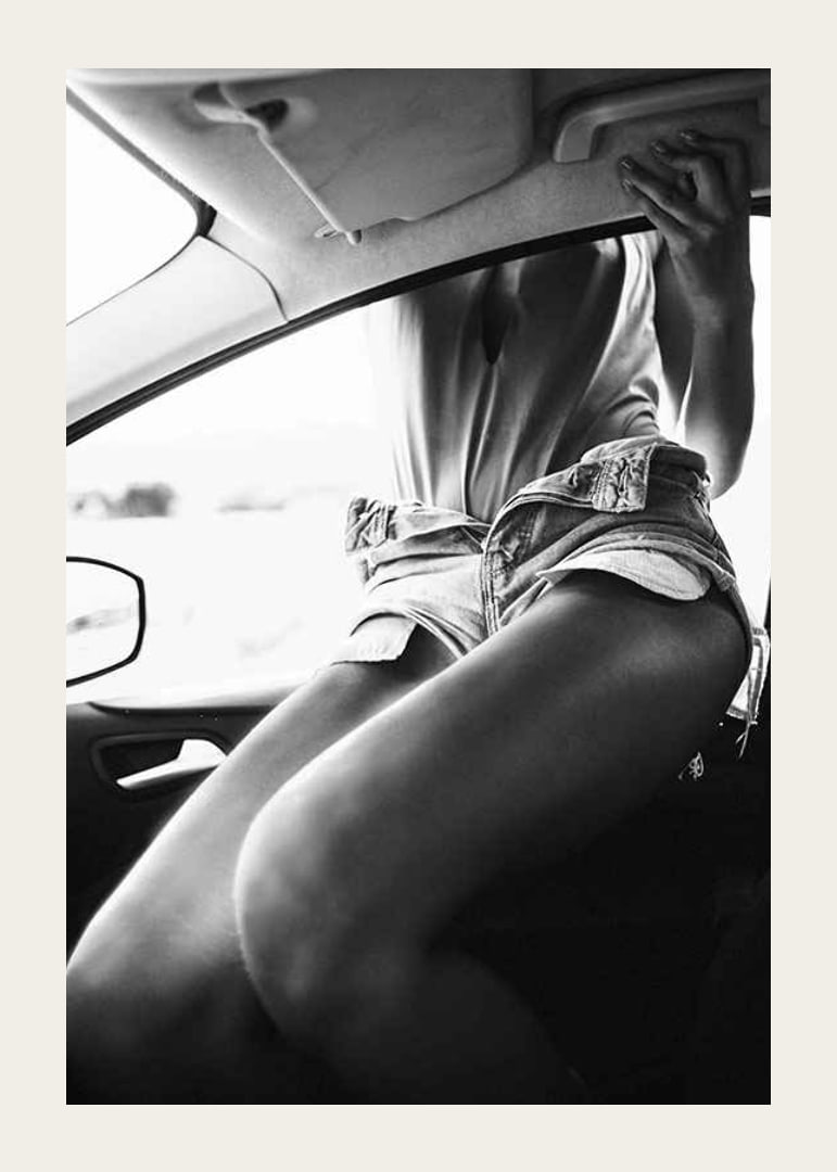 Black and white photo of woman in shorts, sitting in car window-12