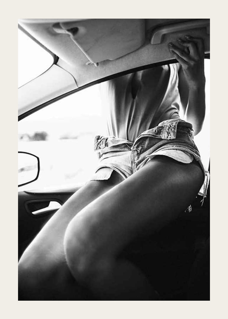 Black and white photo of woman in shorts, sitting in car window-12