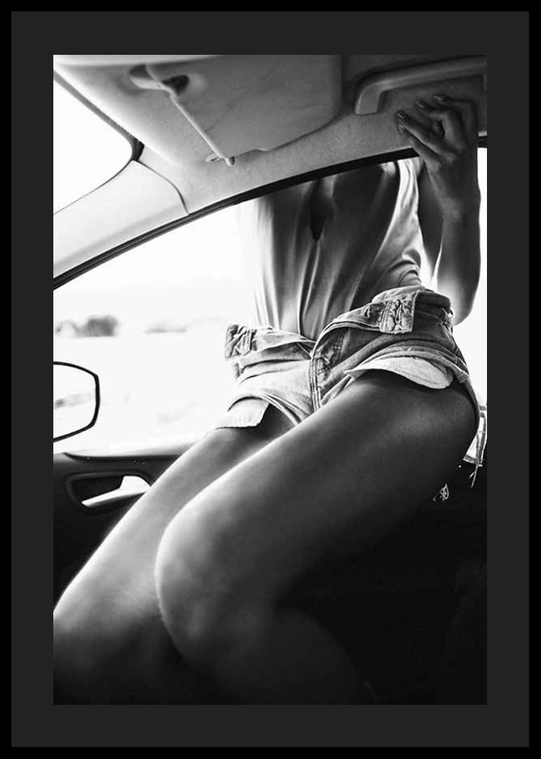Black and white photo of woman in shorts, sitting in car window-12