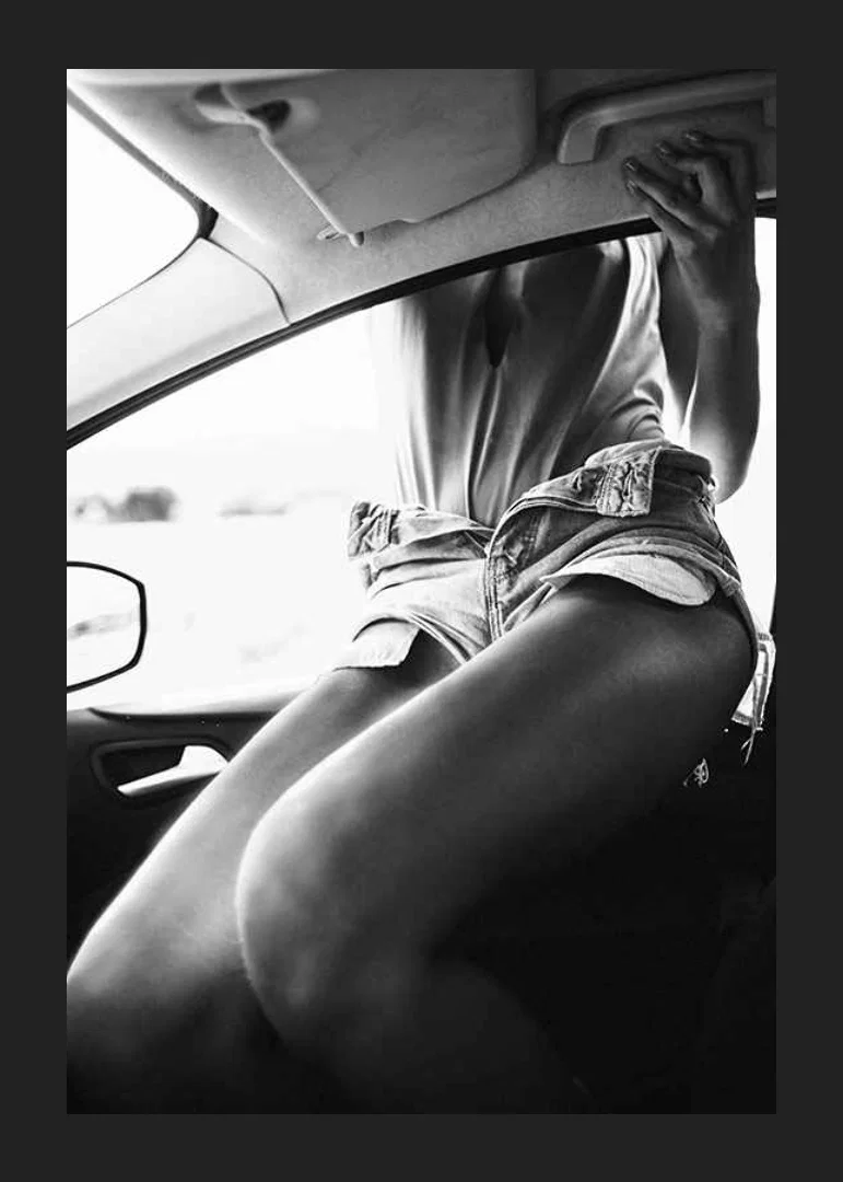 Black and white photo of woman in shorts, sitting in car window-12