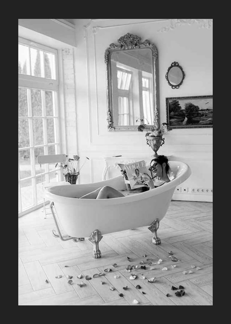 Svartvitt fotografi av kvinna i badkar som läser tidning-12