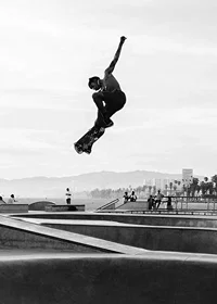 Black and white photograph of skateboarder in the air over skatepark-7