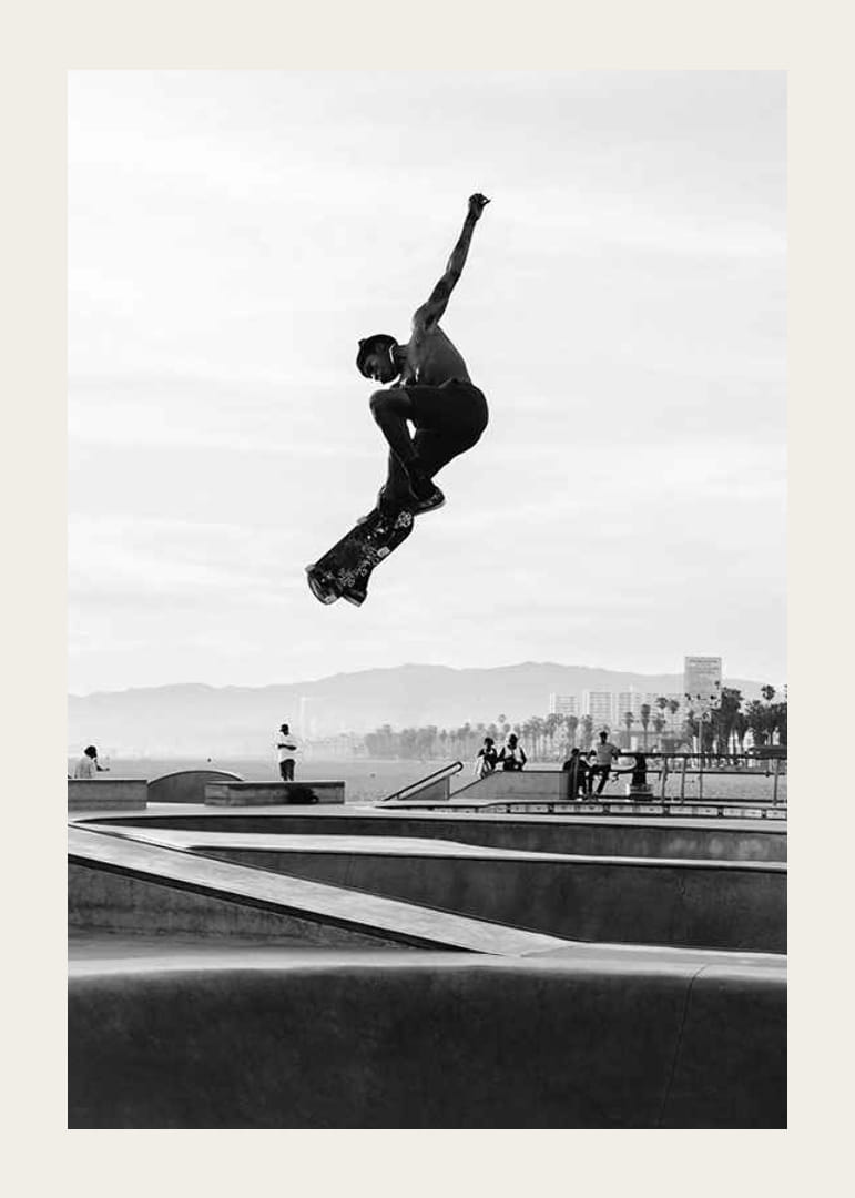 Mustavalkoinen valokuva skeittaajasta ilmassa skeittipuiston yllä-12