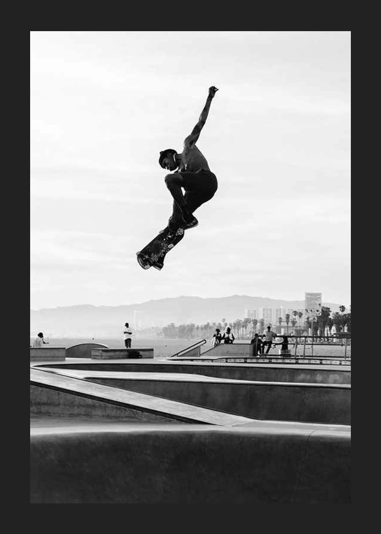 Mustavalkoinen valokuva skeittaajasta ilmassa skeittipuiston yllä-12