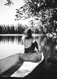 Black and white photograph of woman in boat on calm lake with trees-7