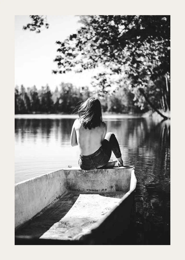 Black and white photograph of woman in boat on calm lake with trees-12
