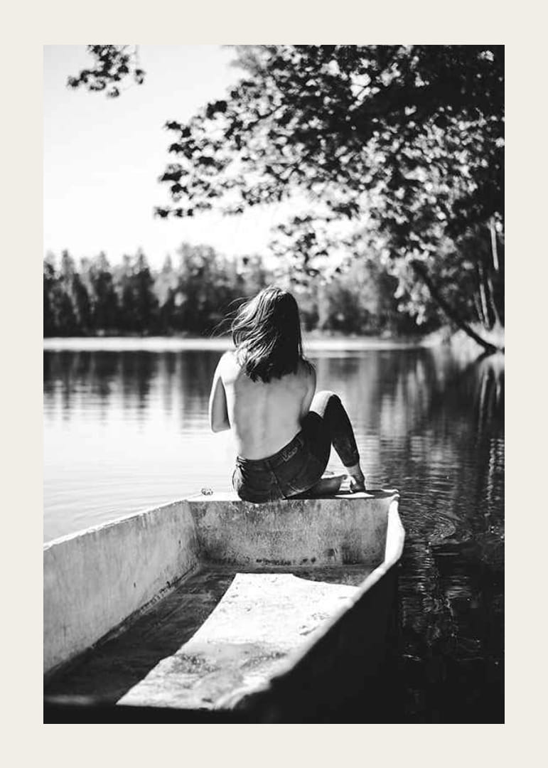 Fotografía en blanco y negro de una mujer en un bote en un lago tranquilo con árboles.-12