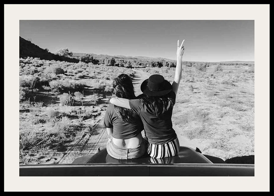 Black and white photograph of two girls on car hood in front of open nature-12
