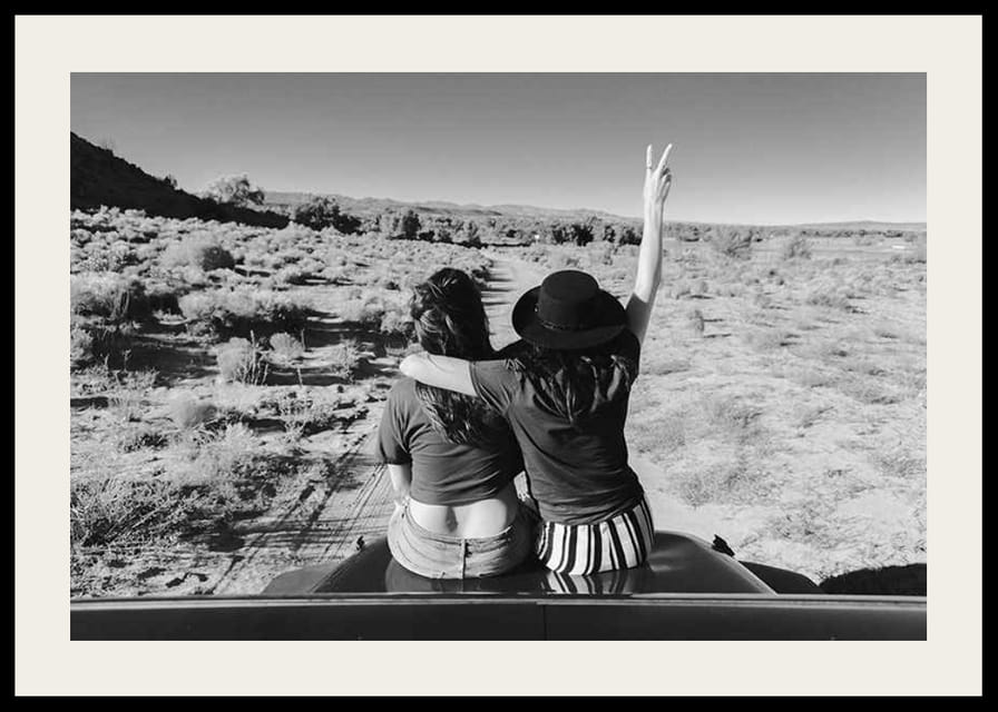 Čiernobiela fotografia dvoch dievčat na kapote auta pred otvorenou prírodou-12