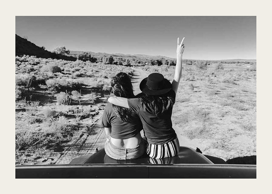 Black and white photograph of two girls on car hood in front of open nature-12