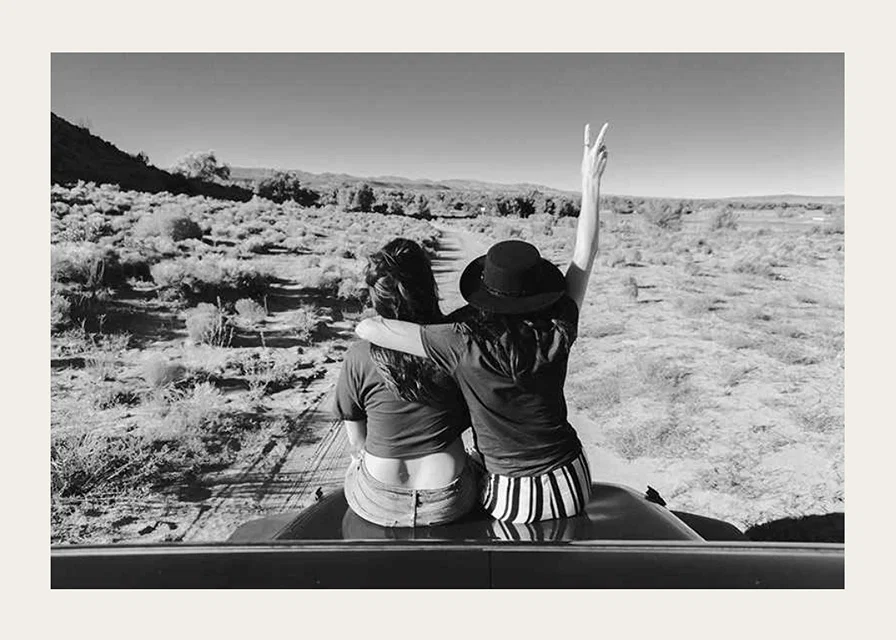 Black and white photograph of two girls on car hood in front of open nature-12