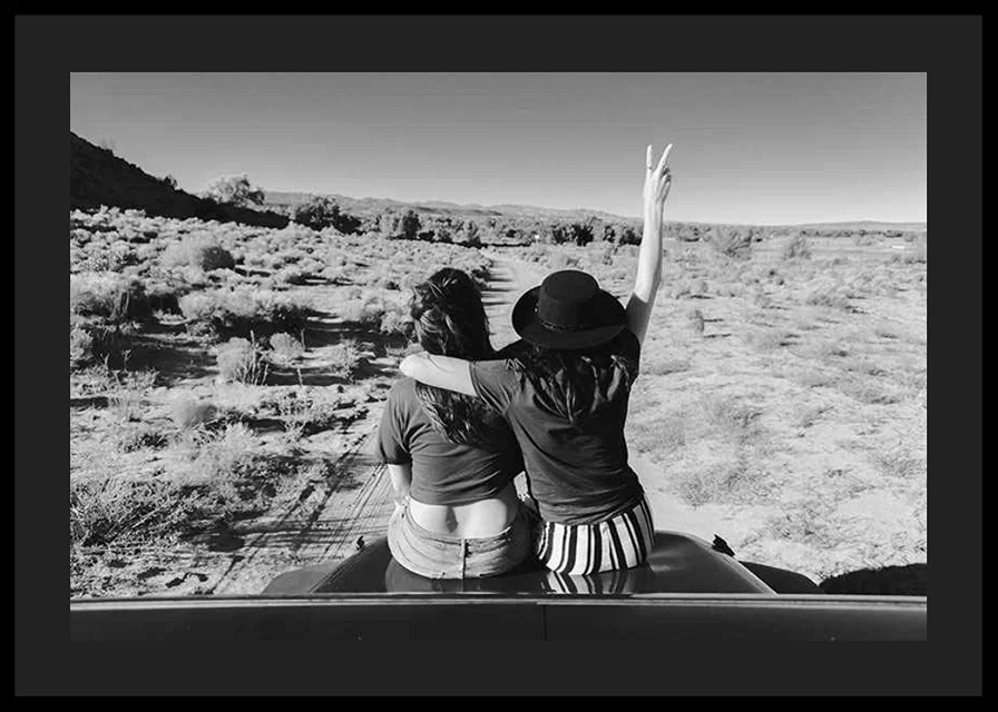 Black and white photograph of two girls on car hood in front of open nature-12