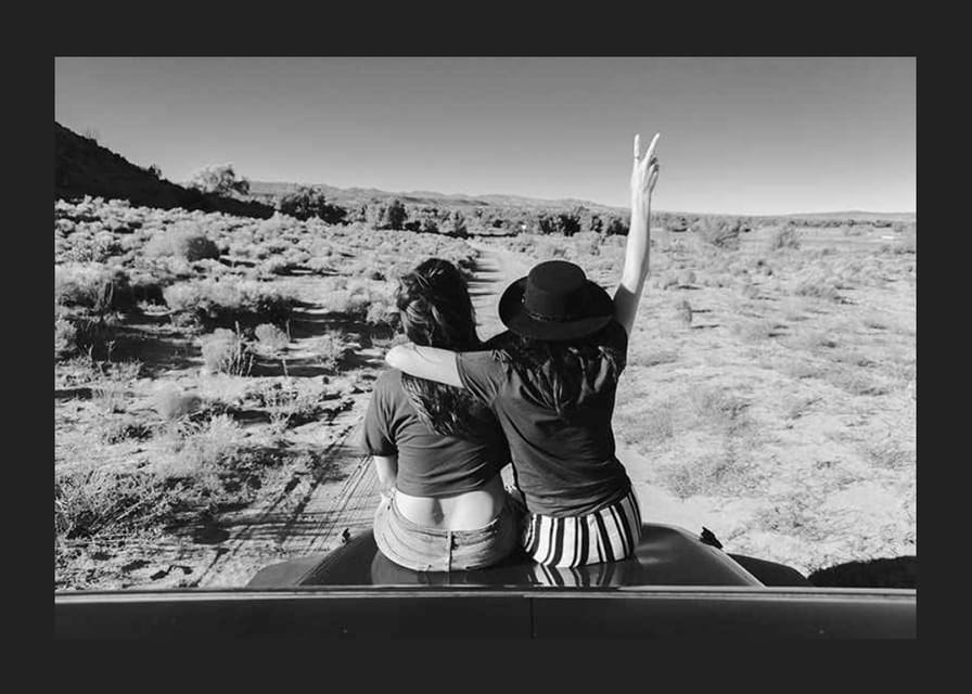 Čiernobiela fotografia dvoch dievčat na kapote auta pred otvorenou prírodou-12