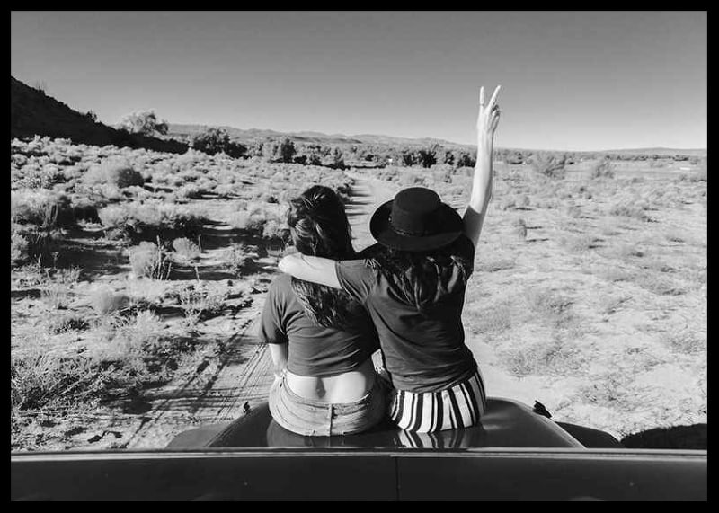 Black and white photograph of two girls on car hood in front of open nature-12