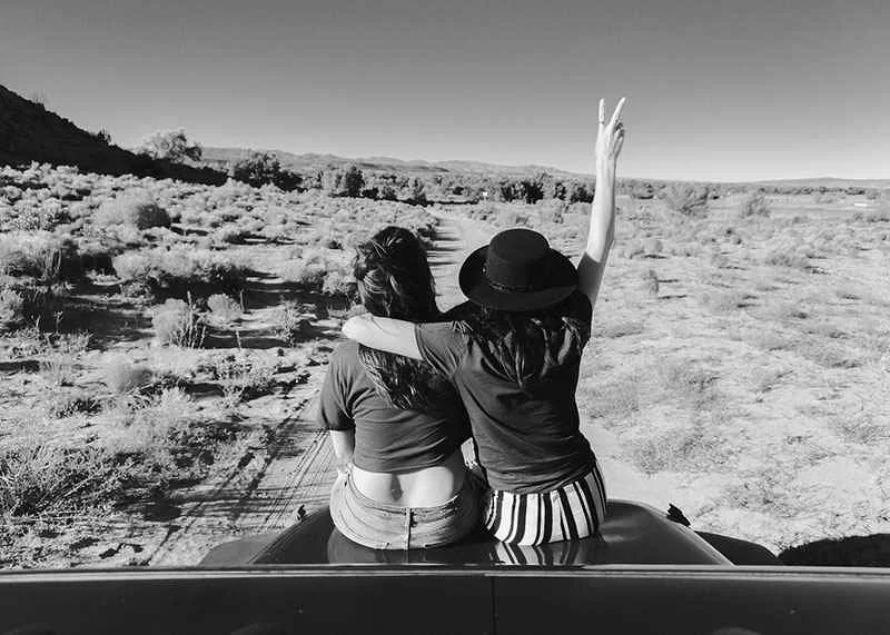 Black and white photograph of two girls on car hood in front of open nature-12