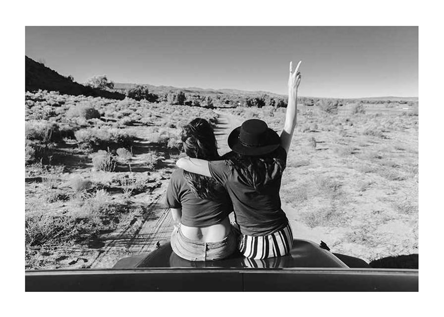Black and white photograph of two girls on car hood in front of open nature-12