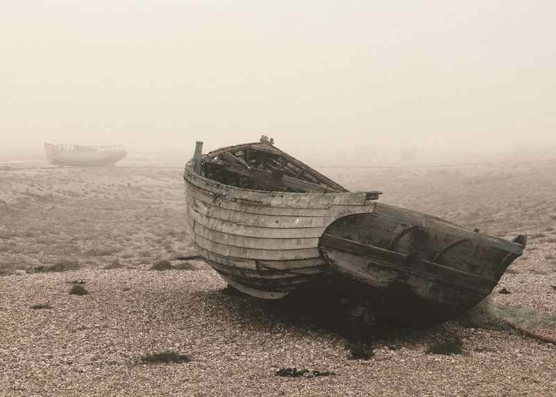 Photograph of old wooden boat on rocky beach in fog-12