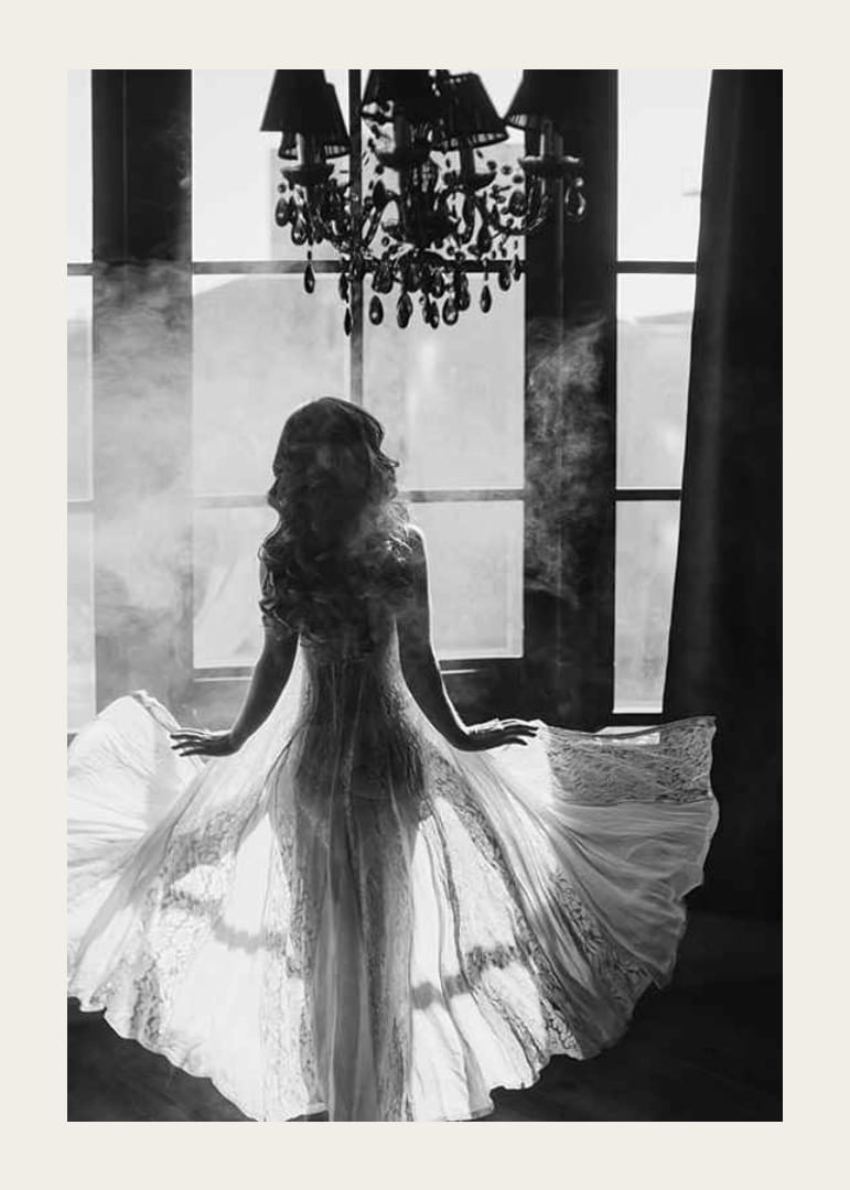 Fekete-fehér fénykép egy csipkeruhás nőről az ablak mellett-12