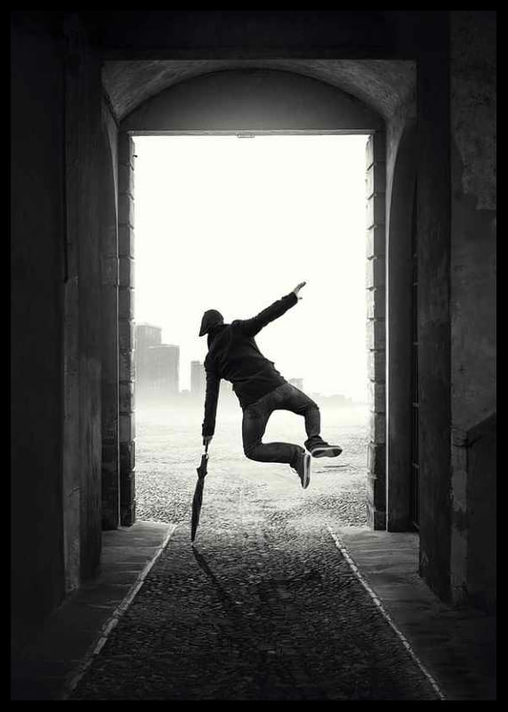 Black and white photograph of jumping man with umbrella in tunnel-12