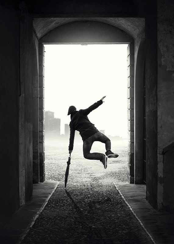 Black and white photograph of jumping man with umbrella in tunnel-12