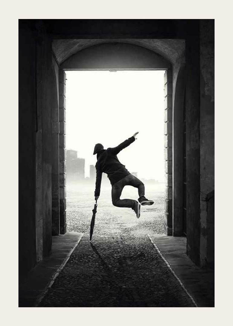 Black and white photograph of jumping man with umbrella in tunnel-12