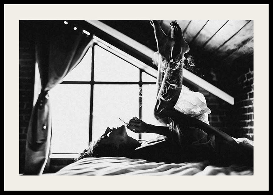 Black and white photograph of woman smoking in bed by window-12