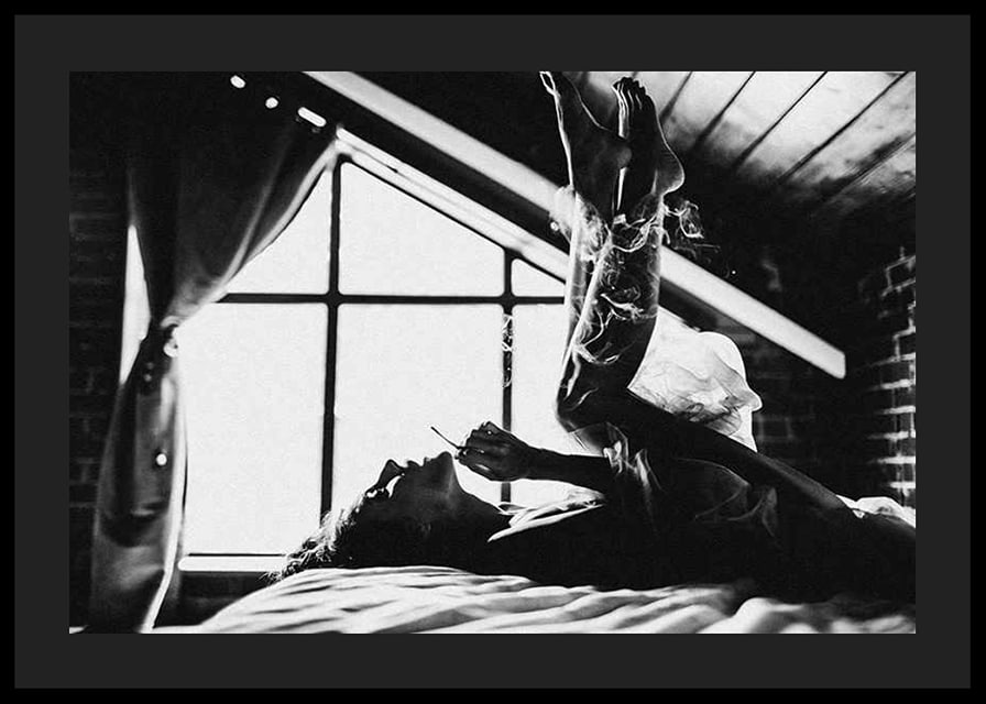 Black and white photograph of woman smoking in bed by window-12