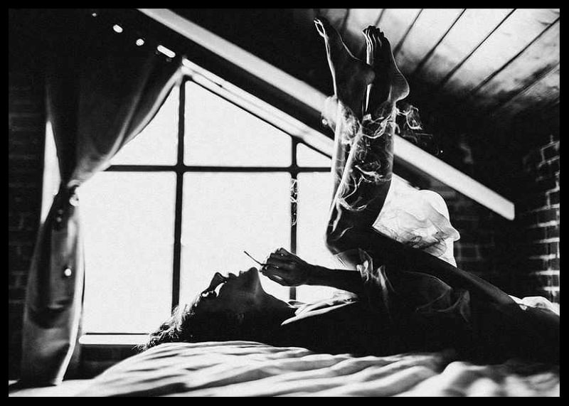 Black and white photograph of woman smoking in bed by window-12