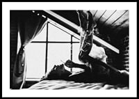 Black and white photograph of woman smoking in bed by window-0