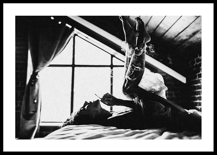 Black and white photograph of woman smoking in bed by window-12