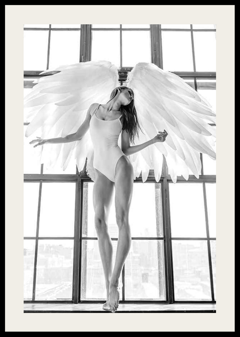 Black and white photo of woman with angel wings by large window-12
