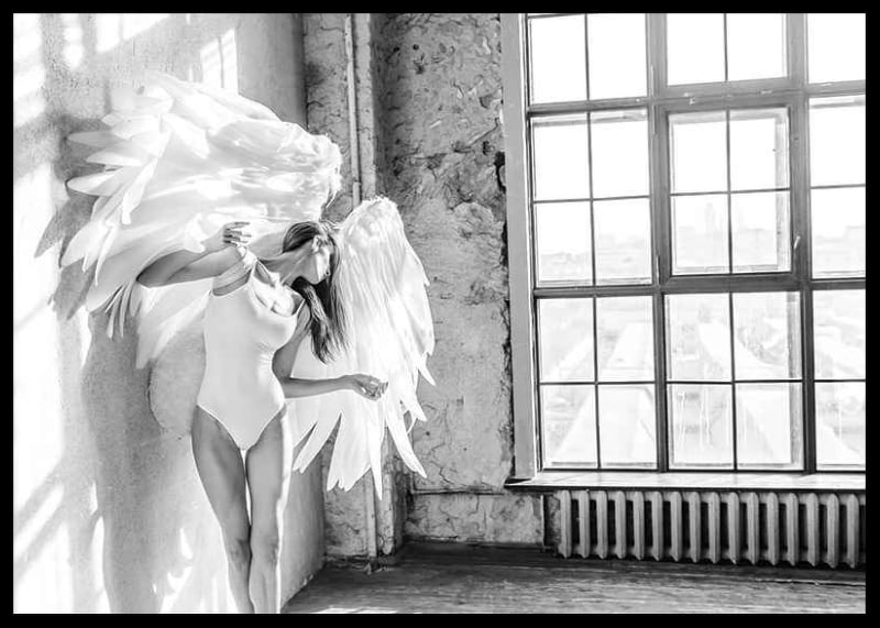 Black and white photo of woman with large angel wings by window-12