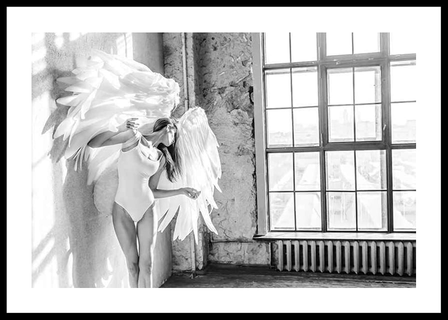 Black and white photo of woman with large angel wings by window-12
