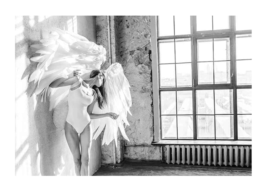 Black and white photo of woman with large angel wings by window-12