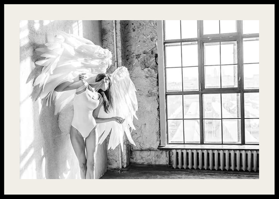 Black and white photo of woman with large angel wings by window-12