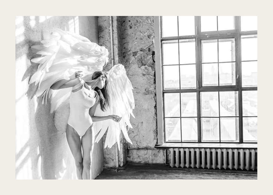 Čiernobiela fotografia ženy s veľkými anjelskými krídlami pri okne-12