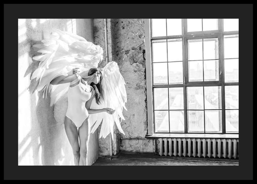 Čiernobiela fotografia ženy s veľkými anjelskými krídlami pri okne-12