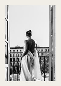 Black and white photo of woman in white dress at open balcony door-3