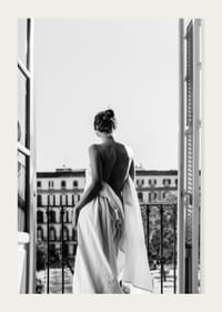 Black and white photo of woman in white dress at open balcony door-3