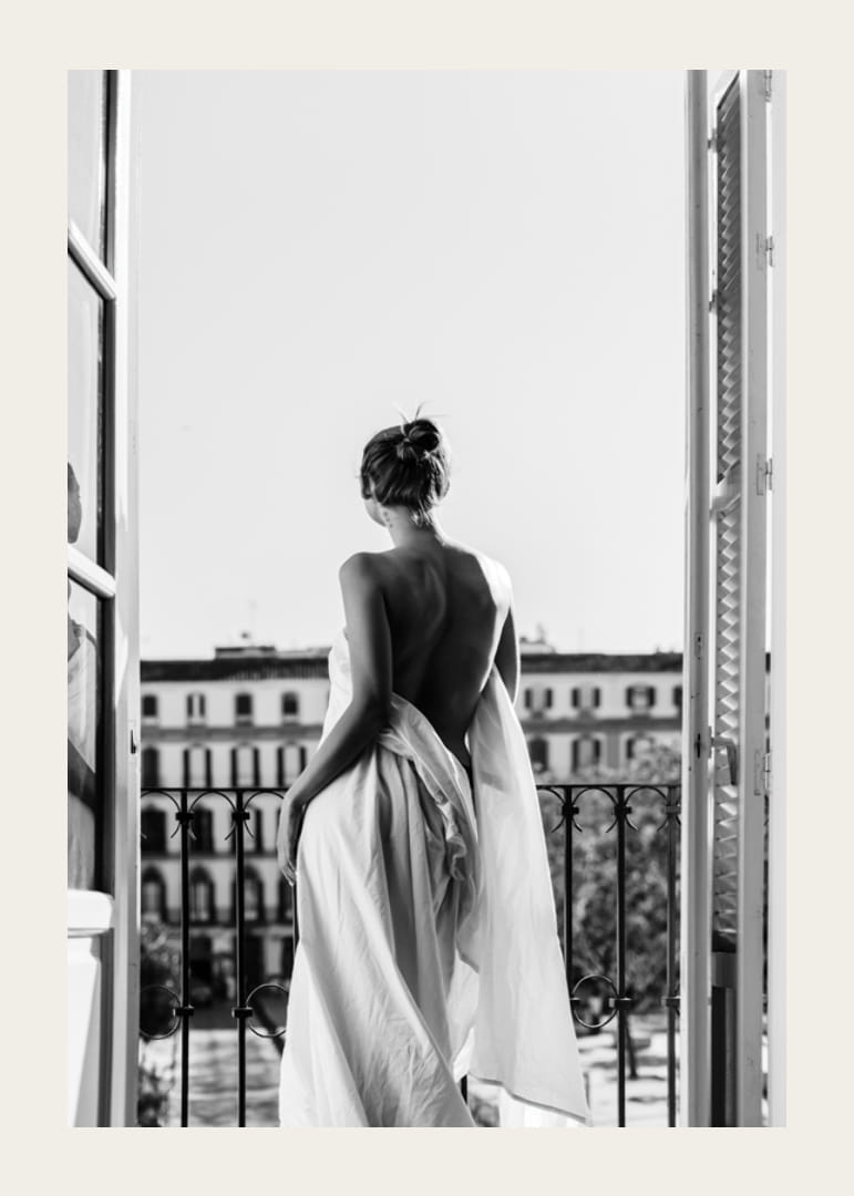 Black and white photo of woman in white dress at open balcony door-12