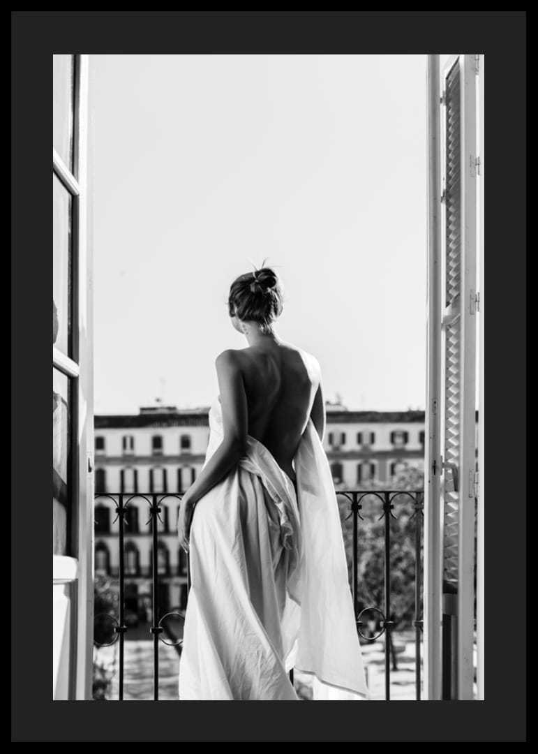 Black and white photo of woman in white dress at open balcony door-12