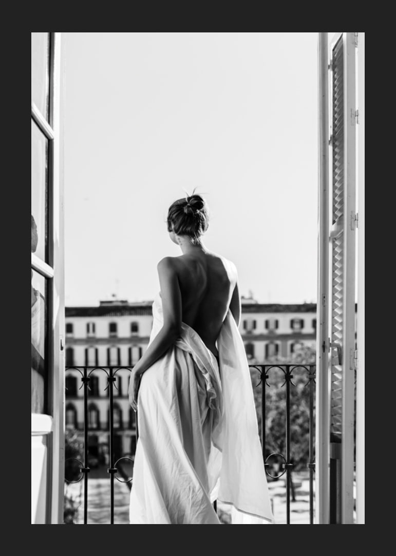 Black and white photo of woman in white dress at open balcony door-12