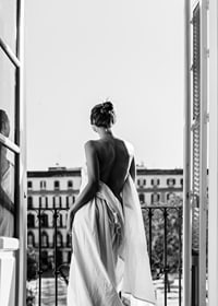 Black and white photo of woman in white dress at open balcony door-7