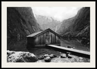 Mustavalkoinen kuva puisesta mökistä järven rannalla, korkeiden vuorten ympäröimänä-2