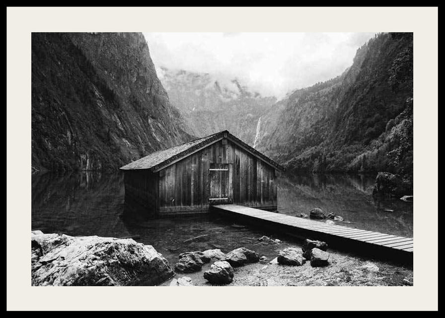 Mustavalkoinen kuva puisesta mökistä järven rannalla, korkeiden vuorten ympäröimänä-12