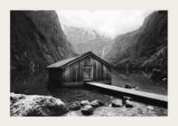 Mustavalkoinen kuva puisesta mökistä järven rannalla, korkeiden vuorten ympäröimänä-3