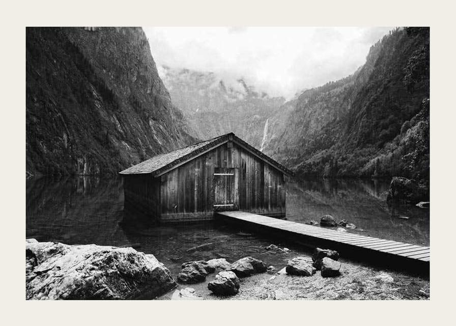 Mustavalkoinen kuva puisesta mökistä järven rannalla, korkeiden vuorten ympäröimänä-12